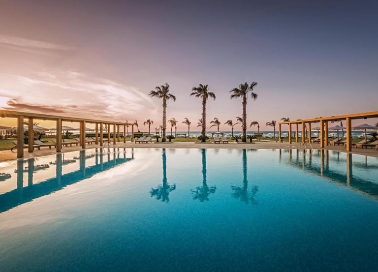 Luxury beachfront swimming pool at a tropical resort with palm trees and a sunset horizon.
