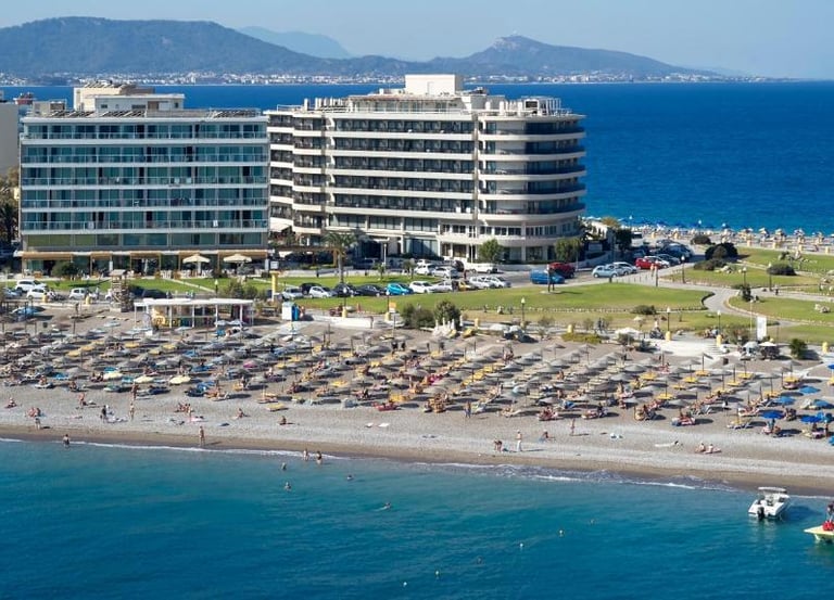 Aerial view of a beach resort in Rhodes, Greece, with waterfront hotels and sun loungers on the sand.
