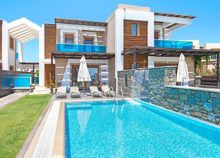 Luxury modern villa with private swimming pool, stone waterfall feature, and sun loungers.