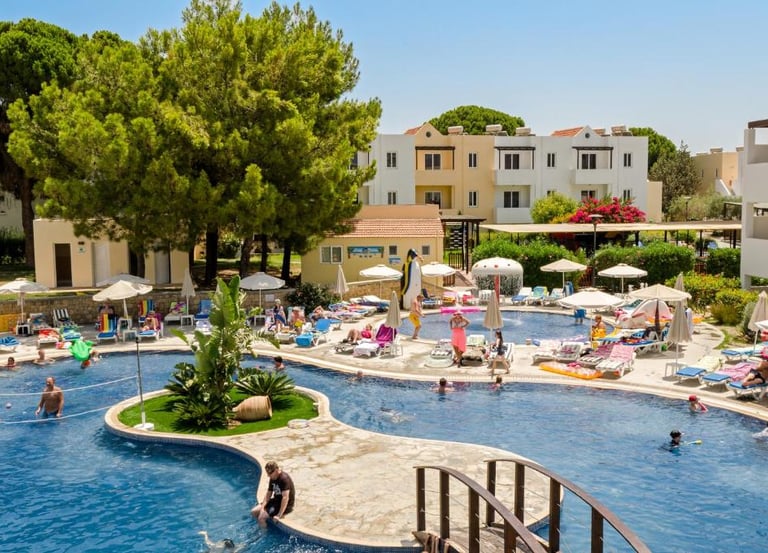 Families relaxing by a large outdoor resort swimming pool with sun loungers and palm trees.