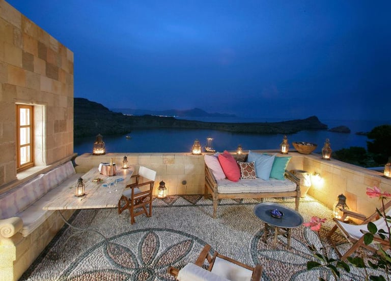 Luxury villa stone terrace with mosaic flooring overlooking a scenic bay at twilight.