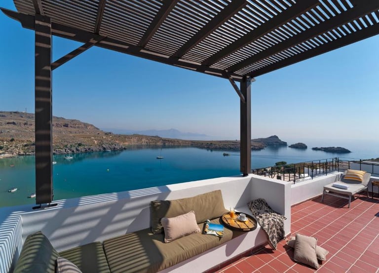 Luxury terrace with pergola and seating overlooking a scenic Mediterranean bay with blue water.