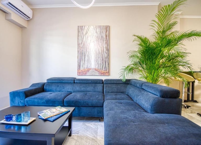 Modern living room featuring a blue sectional sofa, a large palm plant, and forest wall art.