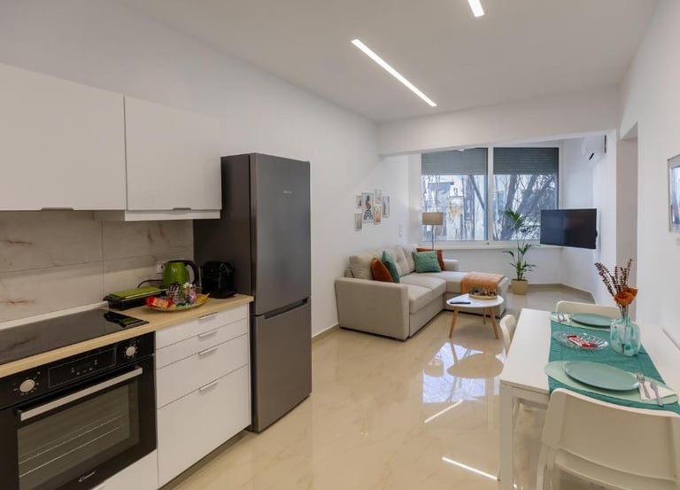 Modern open-plan apartment featuring a sleek kitchenette, gray sofa, and white dining table.