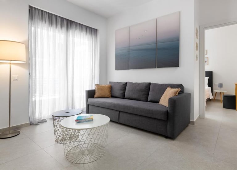 Modern living room featuring a dark grey sofa, round wire coffee tables, and a three-piece ocean wall art.