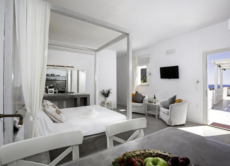 Luxury white hotel suite with a canopy bed, minimalist decor, and a balcony view of the sea.