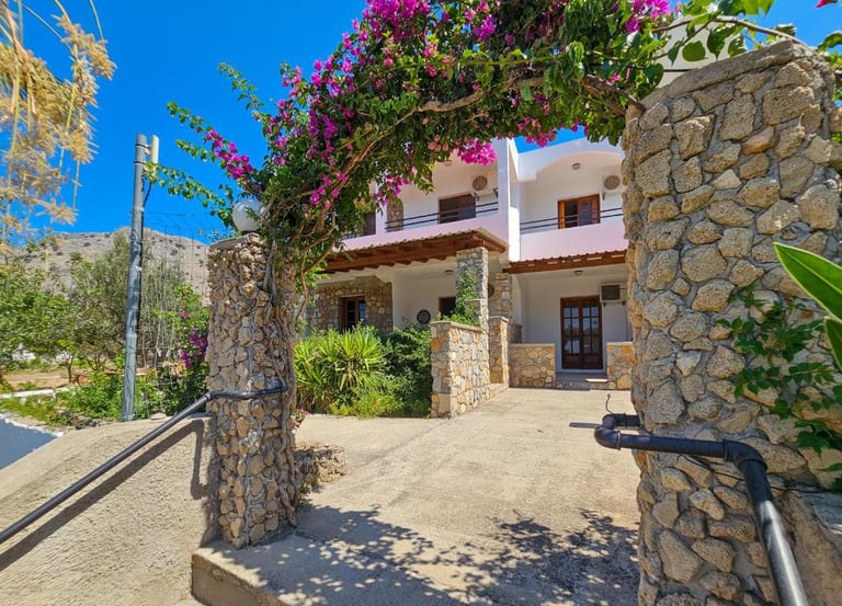 Greek villa entrance with a stone archway covered in blooming purple bougainvillea flowers.