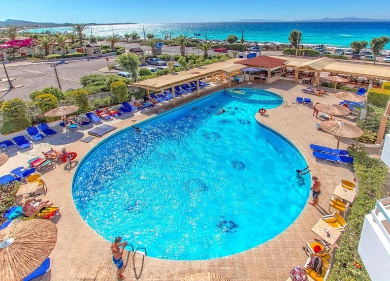 Luxury beach resort with a large outdoor swimming pool, sun loungers, and view of the turquoise Mediterranean sea.