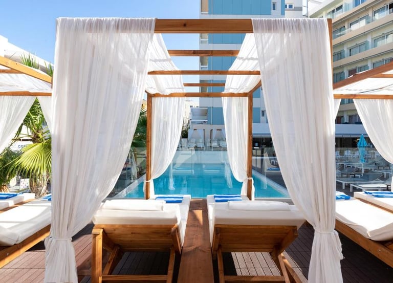 Luxury poolside wooden cabanas with white curtains and sun loungers at a boutique resort hotel.