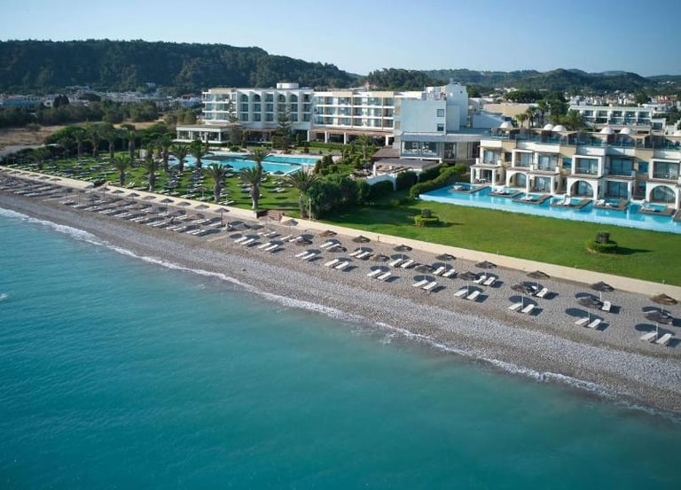 Aerial view of a luxury beachfront resort in Rhodes with swimming pools and a pebble beach.