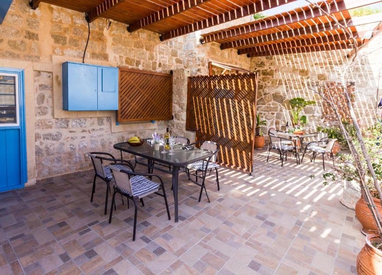 Mediterranean outdoor patio with stone walls, wooden pergola, and dining sets for al fresco meals.