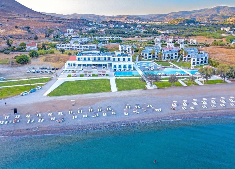 Aerial view of a luxury beachfront resort in Greece with outdoor swimming pools and a pebble beach.