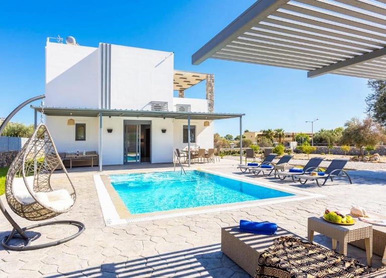Luxury white villa with private swimming pool, sun loungers, and hanging egg chair.