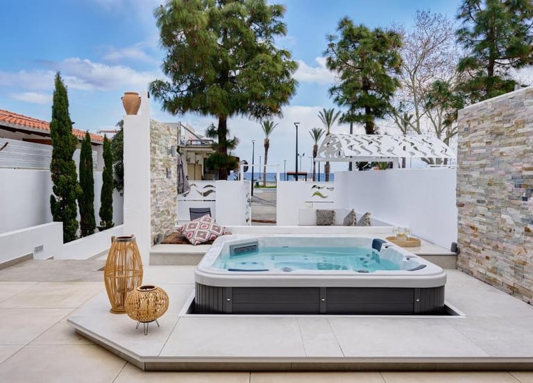 Luxury outdoor patio featuring a modern hot tub, white stone walls, and Mediterranean landscaping.