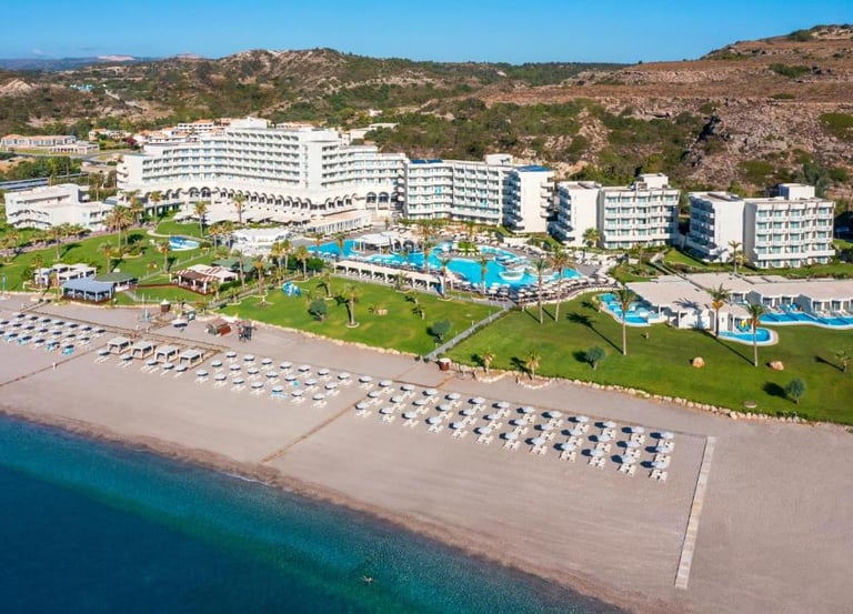 Aerial view of a luxury beachfront resort with swimming pools, white umbrellas, and turquoise ocean water.