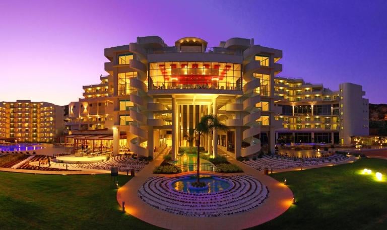 Luxury five-star beach resort hotel illuminated at sunset with modern architecture and gardens.