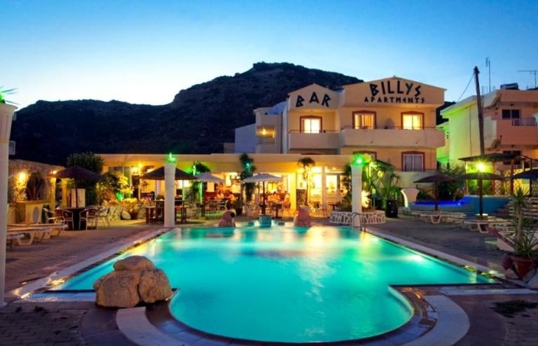 Illuminated swimming pool at Billy's Apartments and Bar in Greece at twilight.