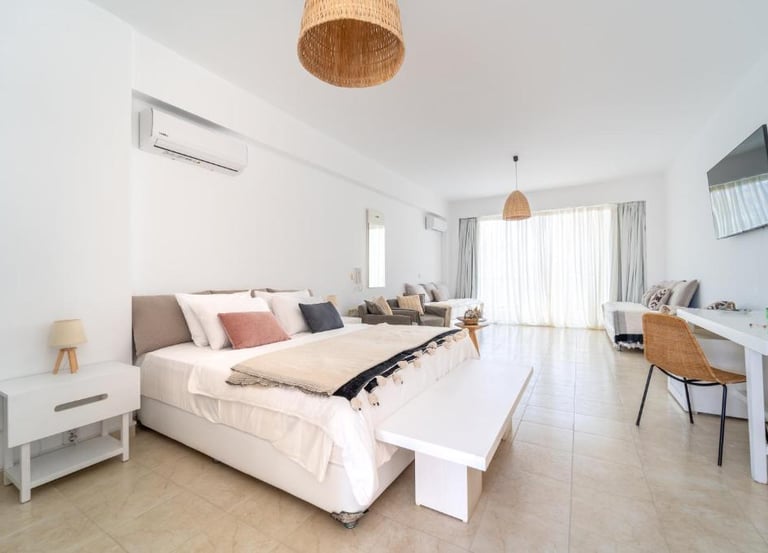 Modern white hotel suite with a king-size bed, air conditioning, and a bright living area.