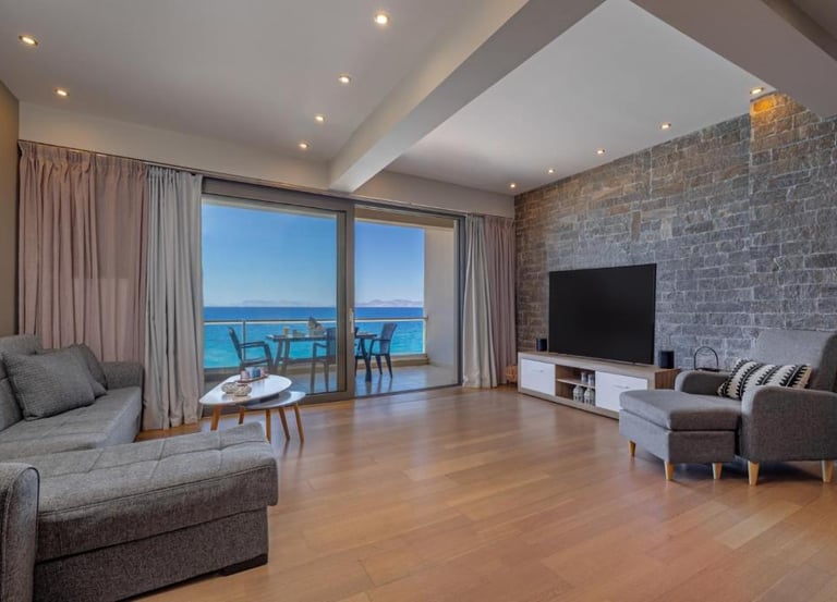 Modern living room with a stone wall, grey sofa, and balcony overlooking the blue ocean.