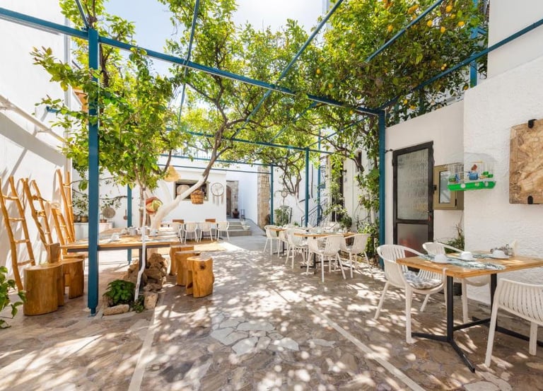 Sun-drenched Mediterranean outdoor restaurant patio featuring a lush lemon tree canopy and stone flooring.