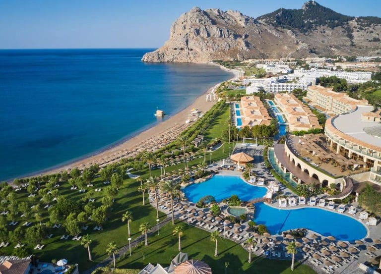 Aerial view of a luxury beachfront resort in Rhodes, Greece with swimming pools and sandy beach.