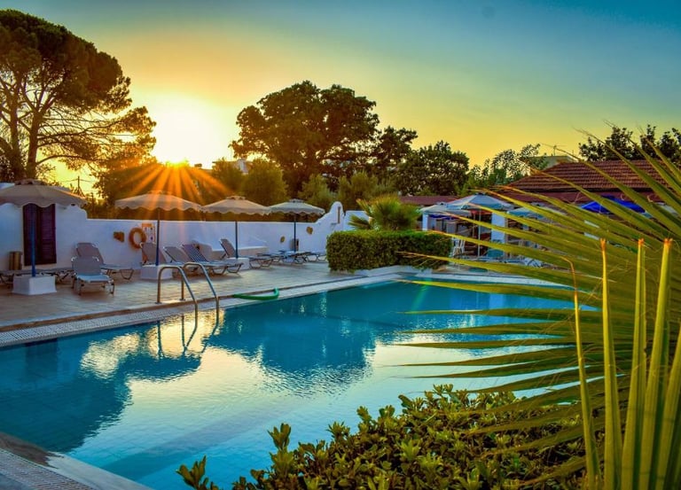 Luxury hotel swimming pool with lounge chairs and umbrellas during a vibrant golden hour sunset.
