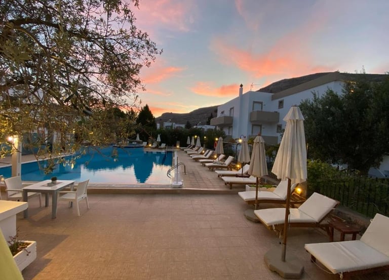 Luxury resort swimming pool with lounge chairs and umbrellas at sunset in Greece.