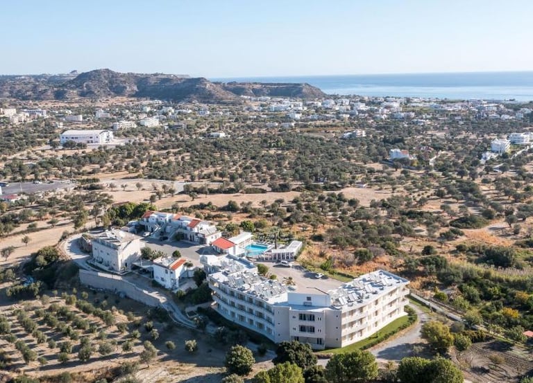 Aerial view of a white luxury hotel resort nestled in a lush olive grove overlooking the Mediterranean coast.