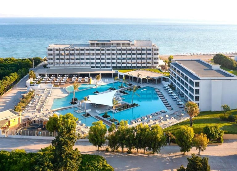 Luxury beachfront resort with a large swimming pool, lounge chairs, and ocean views in Greece.