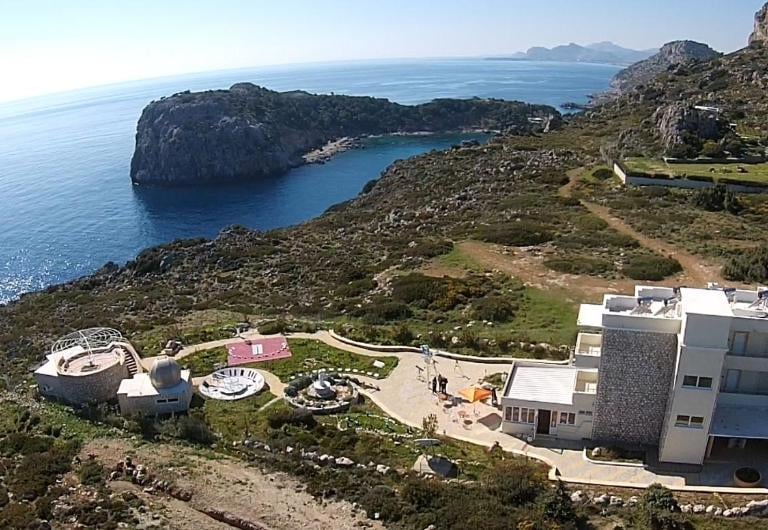 Aerial view of a coastal observatory and villa on a rocky cliff overlooking the Aegean Sea.