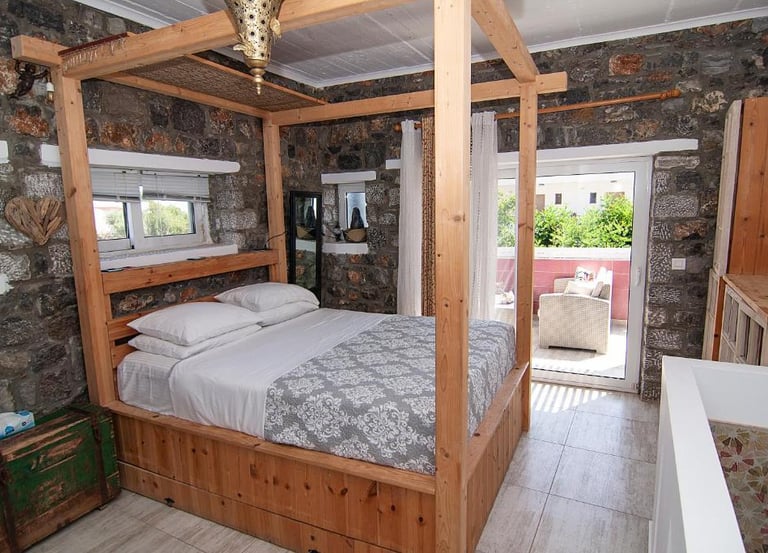 Rustic bedroom featuring a wooden canopy bed, stone walls, and a private balcony.