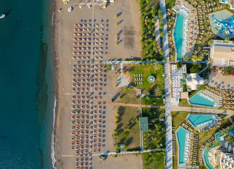 Aerial view of a luxury beachfront resort with swimming pools and sand beach umbrellas.