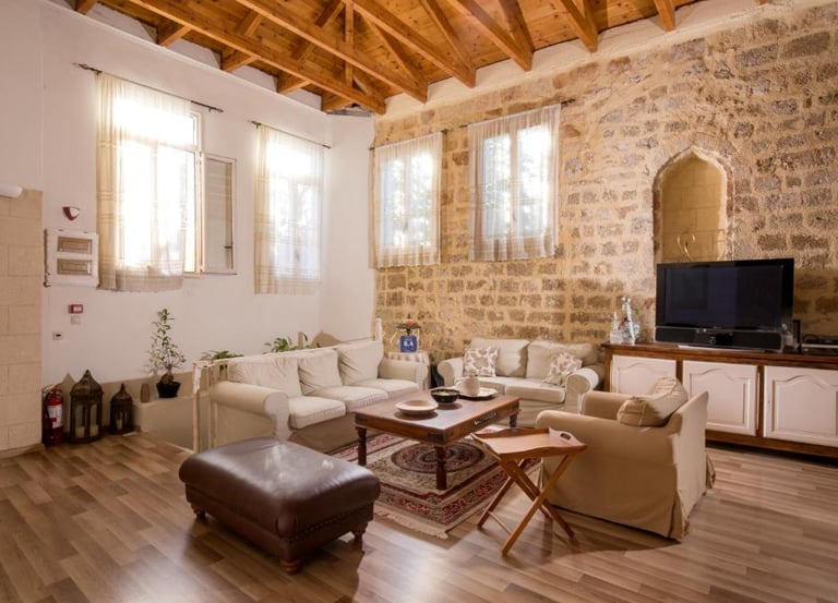 Rustic living room with exposed stone walls, wooden ceiling beams, and comfortable white sofas.