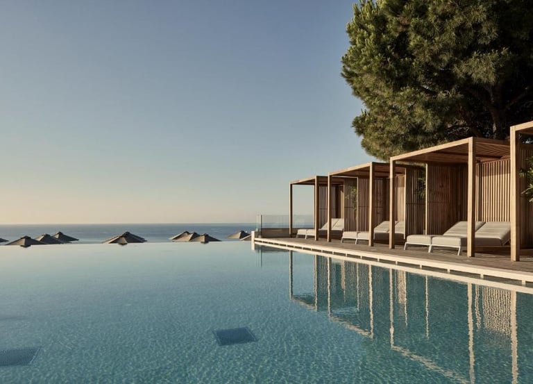 Luxury infinity pool with wooden cabanas and lounge chairs overlooking the ocean at a boutique resort.