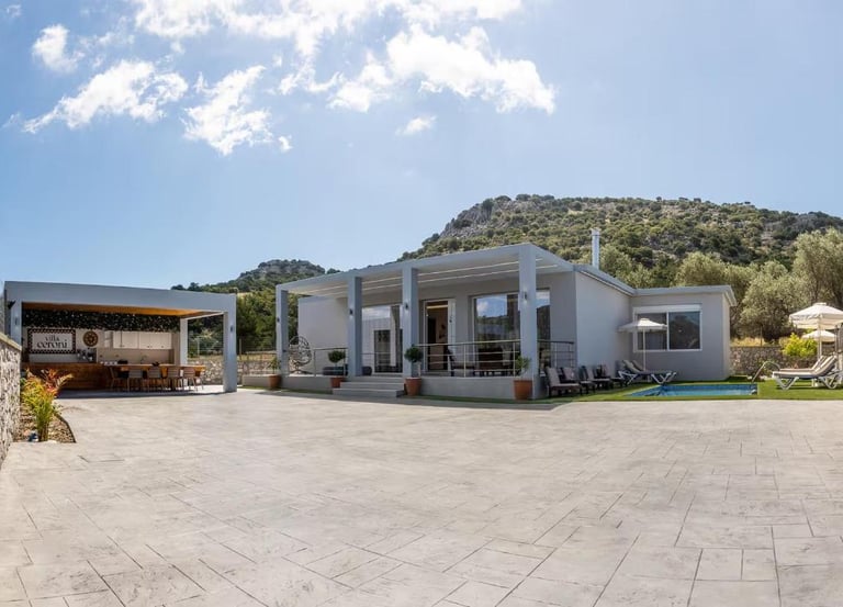 Luxury modern villa with private pool, outdoor kitchen, and mountain views under a sunny sky.