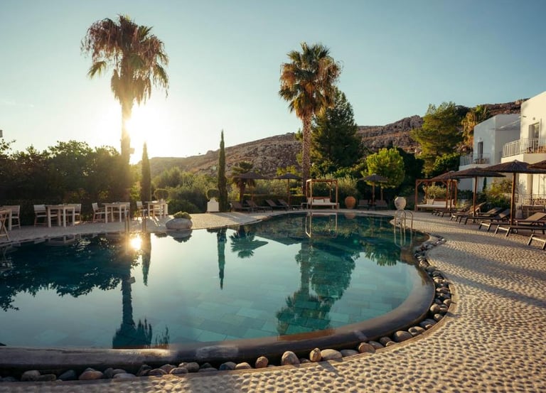 Luxury outdoor swimming pool at a Mediterranean resort with palm trees and lounge chairs at sunset.