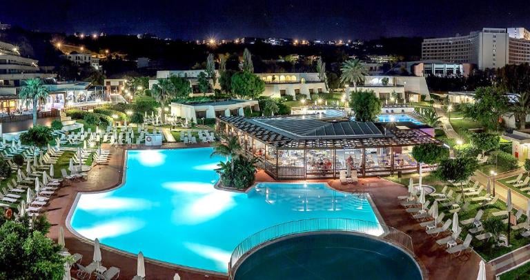Night view of a luxury beachfront resort with illuminated swimming pools and lounge areas.