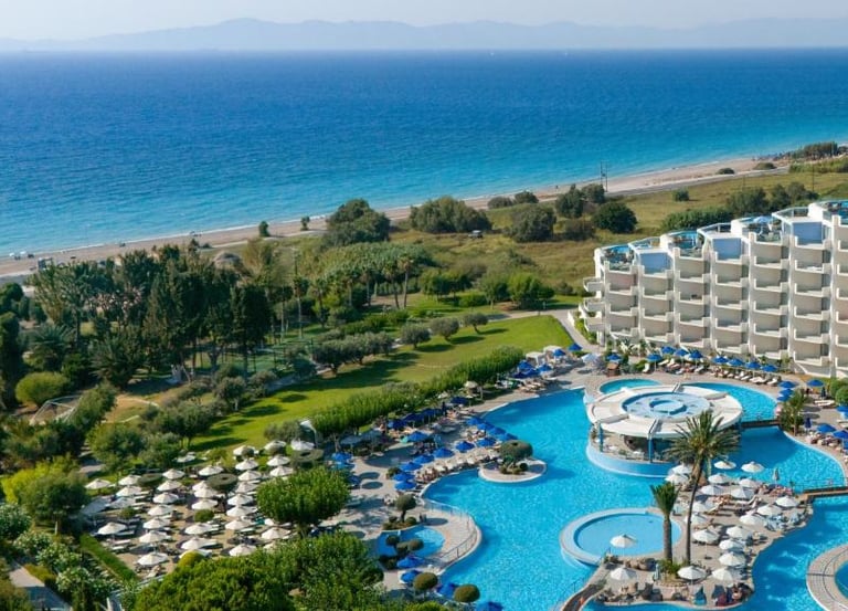 Luxury beach resort with blue swimming pools, sun loungers, and ocean views in Greece.