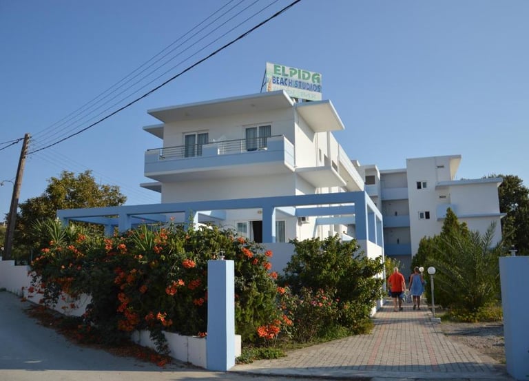 Exterior view of Elpida Beach Studios hotel in Greece with white architecture and blooming flowers.