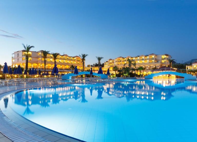 Luxury resort swimming pool with illuminated hotel buildings and palm trees at dusk.