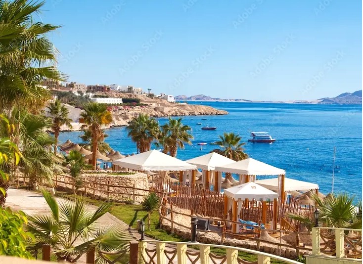 Praia de areia branca em Hurghada com resorts de luxo em frente ao Mar Vermelho turquesa. Ao fundo, a Marina de Hurghada