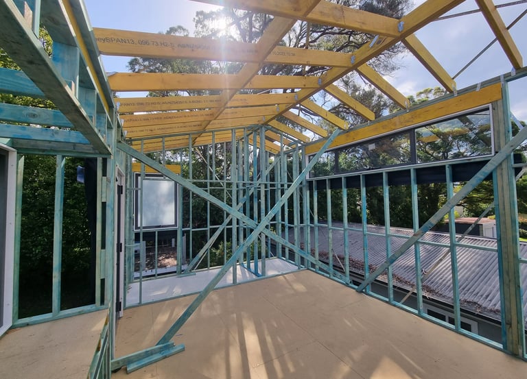 Construction site showing timber roof trusses and wall framing for a new house addition.