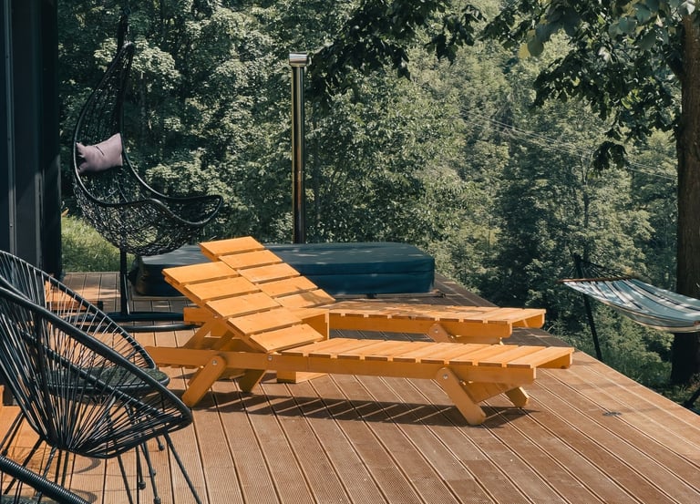 Modern wooden deck with yellow lounge chairs, a hot tub, and a hanging chair overlooking a lush forest.