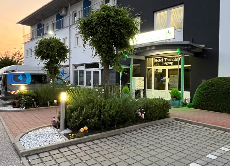 The exterior entrance of Hotel Thannhof at sunset with a paved parking area and green landscaping.