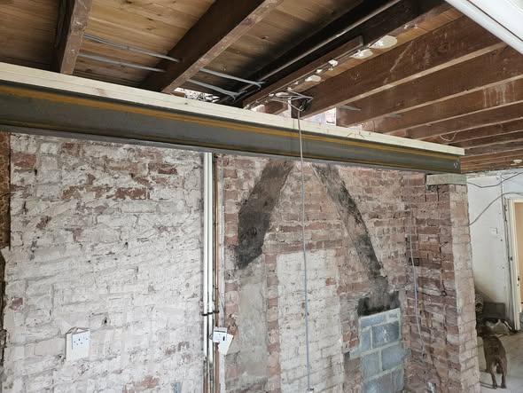 A structural steel RSJ beam installed against a red brick wall during a home renovation.