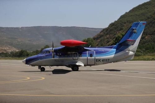 A blue and white Nov Air Let L-410 Turbolet airplane taxiing on an airport runway.
