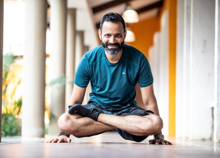 Smiling yoga instructor performing an advanced arm balance pose in a bright studio hallway.