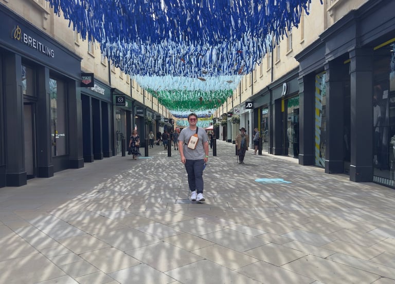 A person walks through an outdoor shopping mall under a blue hanging ribbon art installation.