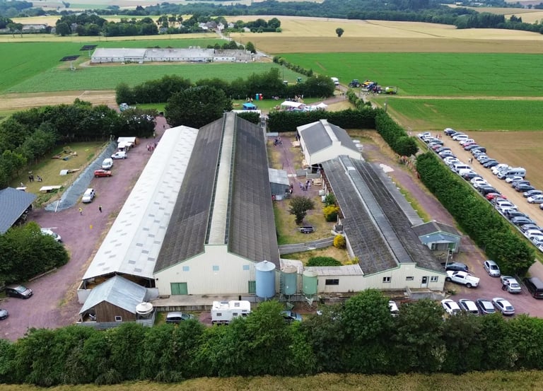 Vue aérienne d'un événement agricole avec de grandes granges industrielles, un parking et des champs
