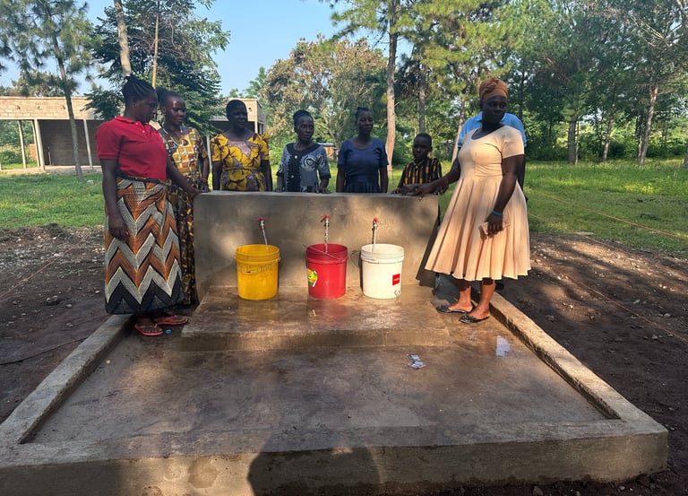 African women standing around a community water tap station with buckets for clean water access.